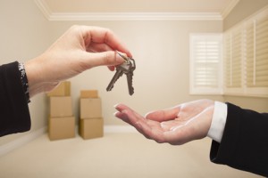 Woman Handing Over the House Keys To A New Home Inside Empty Tan Colored Room.